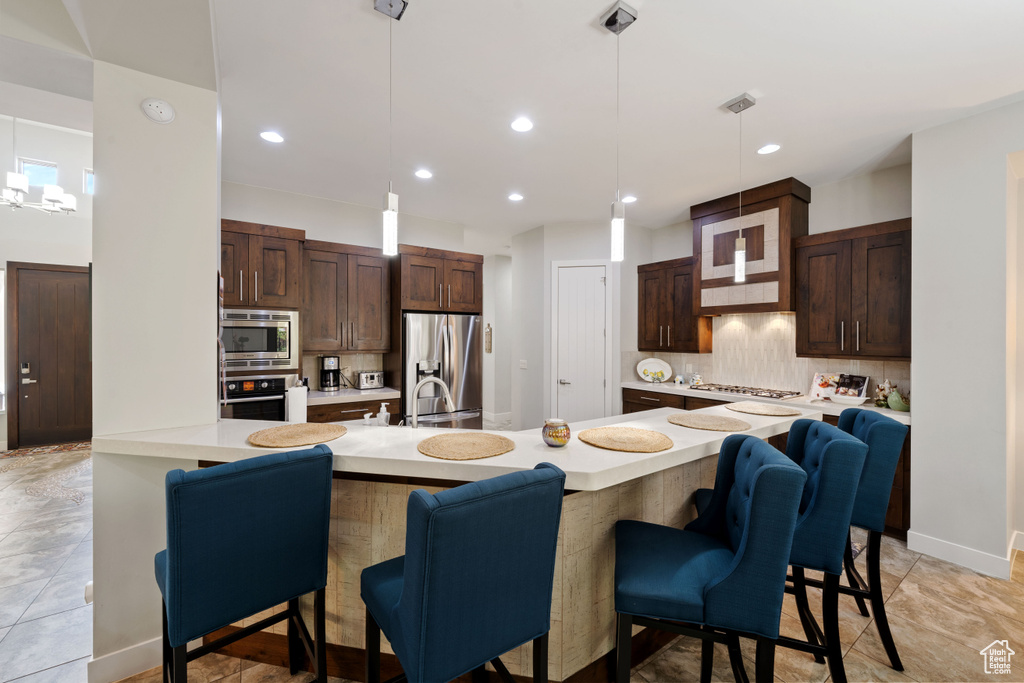 Kitchen featuring decorative backsplash, light countertops, a breakfast bar area, and appliances with stainless steel finishes