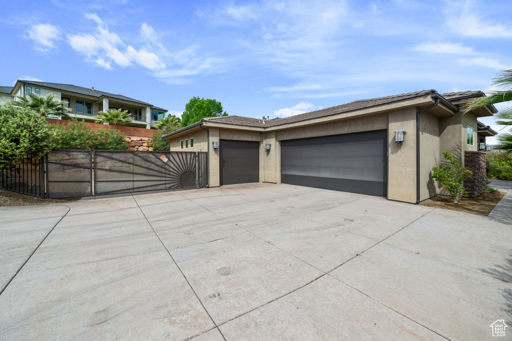 View of front facade featuring stucco siding, an attached garage, concrete driveway, and a gate