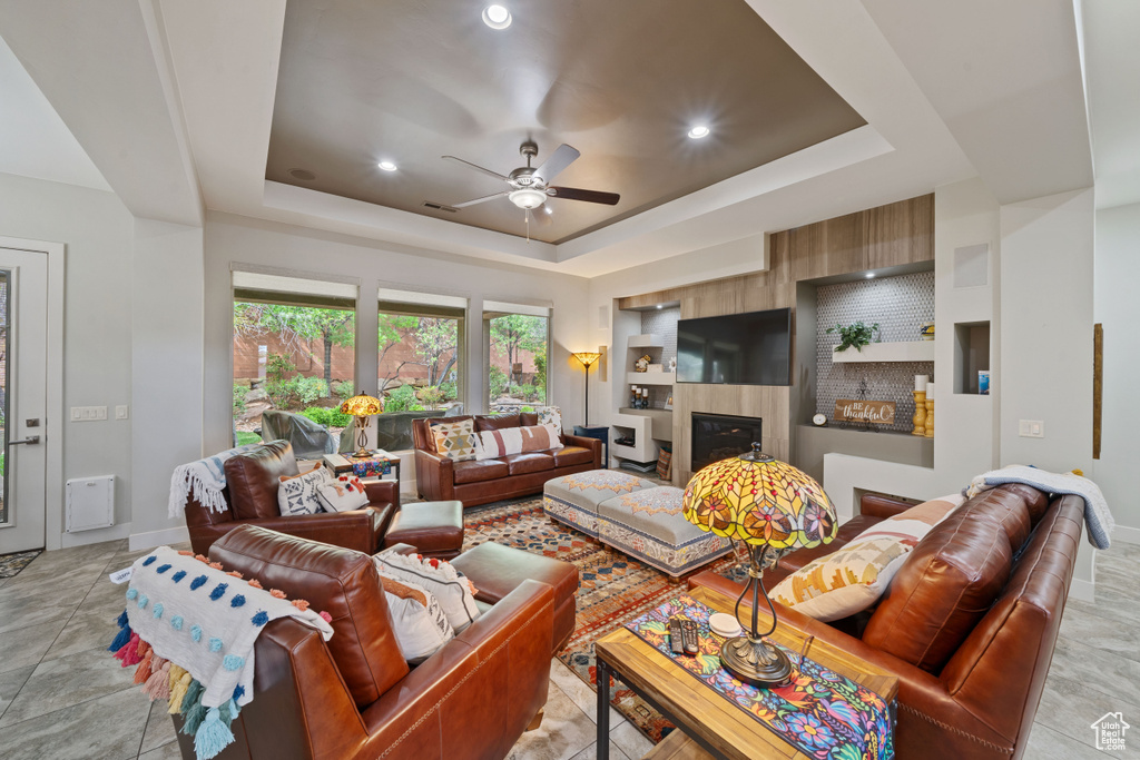 Living area with a tile fireplace, baseboards, a raised ceiling, and ceiling fan