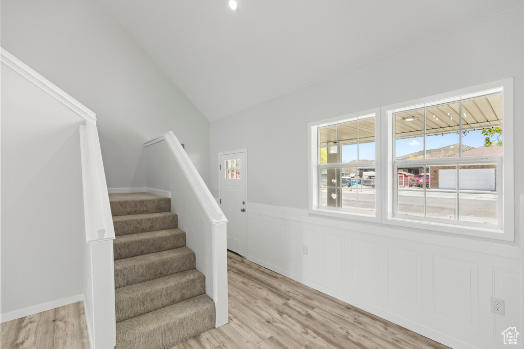 Staircase with a wainscoted wall, wood finished floors, a healthy amount of sunlight, and vaulted ceiling