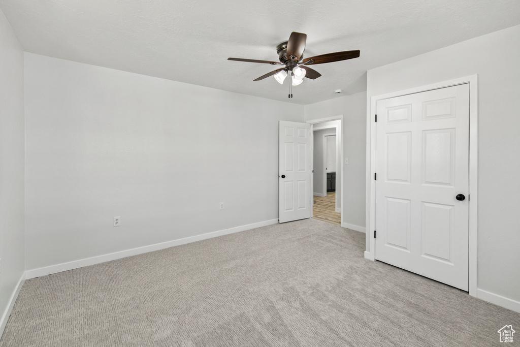 Unfurnished bedroom with light carpet, a ceiling fan, and baseboards
