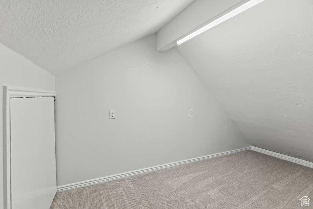 Bonus room featuring baseboards, a textured ceiling, lofted ceiling, and carpet floors