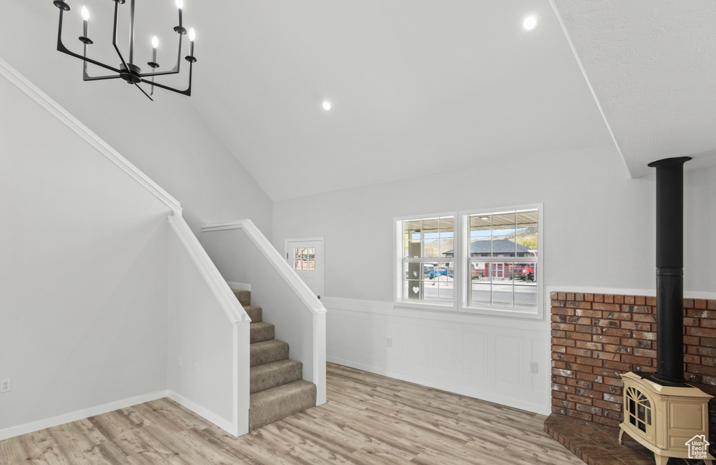 Interior space with a wood stove, stairway, a notable chandelier, a wainscoted wall, and wood finished floors