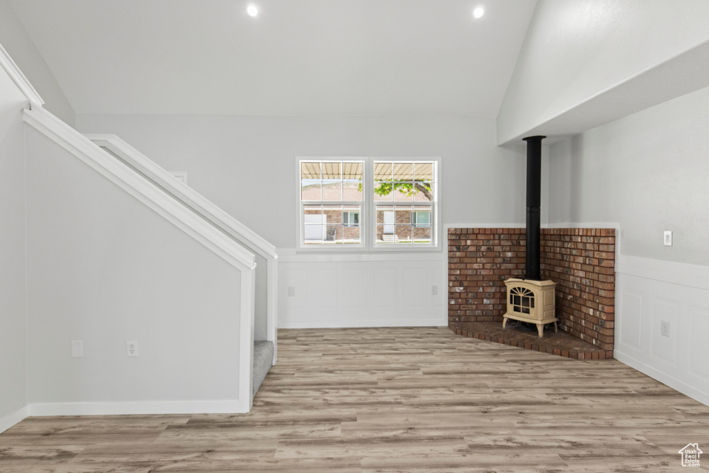 Unfurnished living room with light wood-style floors, a wainscoted wall, stairway, a wood stove, and lofted ceiling