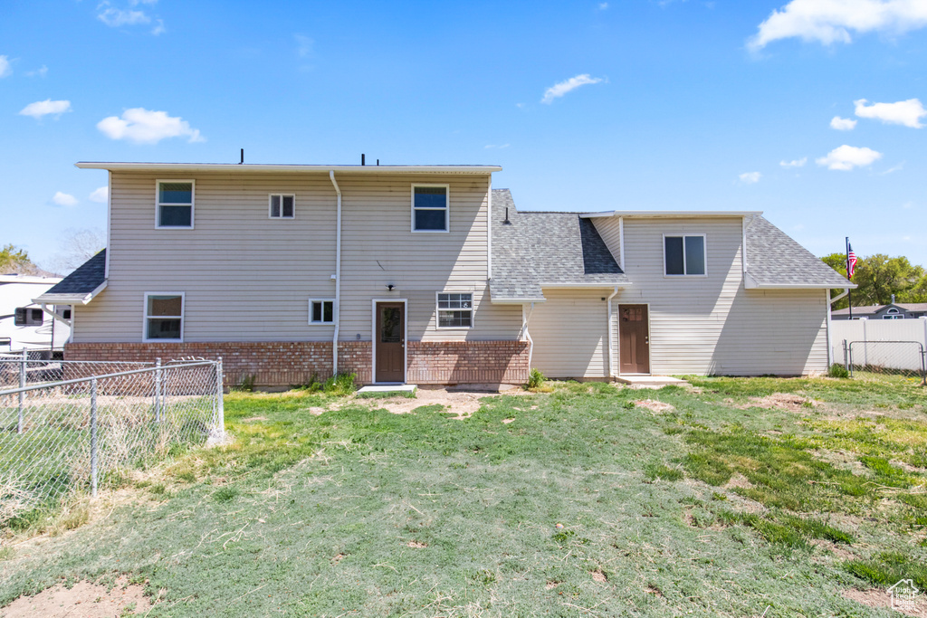 Back of property with a lawn, a shingled roof, brick siding, and fence