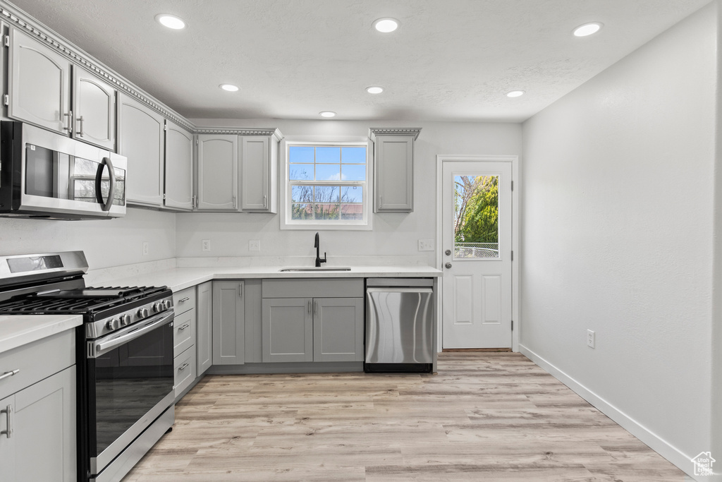 Kitchen with recessed lighting, a sink, light wood-type flooring, gray cabinetry, and appliances with stainless steel finishes
