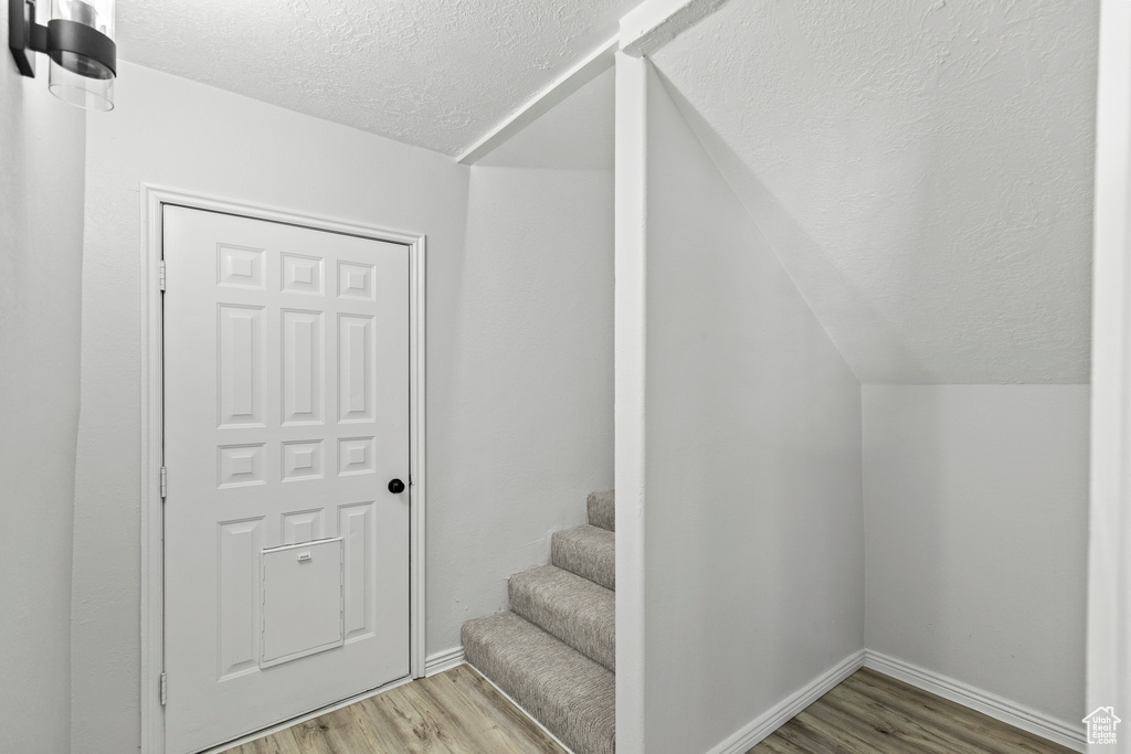 Staircase with baseboards, wood finished floors, a textured ceiling, and lofted ceiling