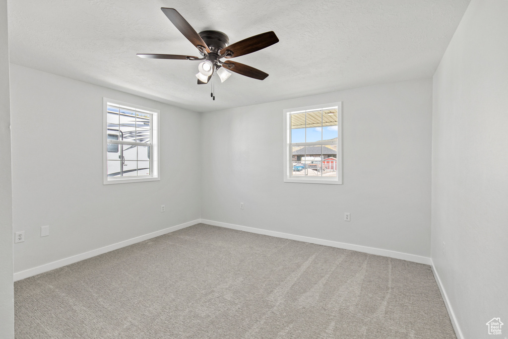 Carpeted spare room featuring a textured ceiling, a ceiling fan, and baseboards