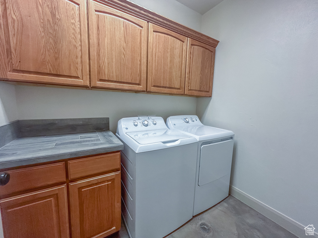 Clothes washing area with washing machine and dryer, baseboards, and cabinet space