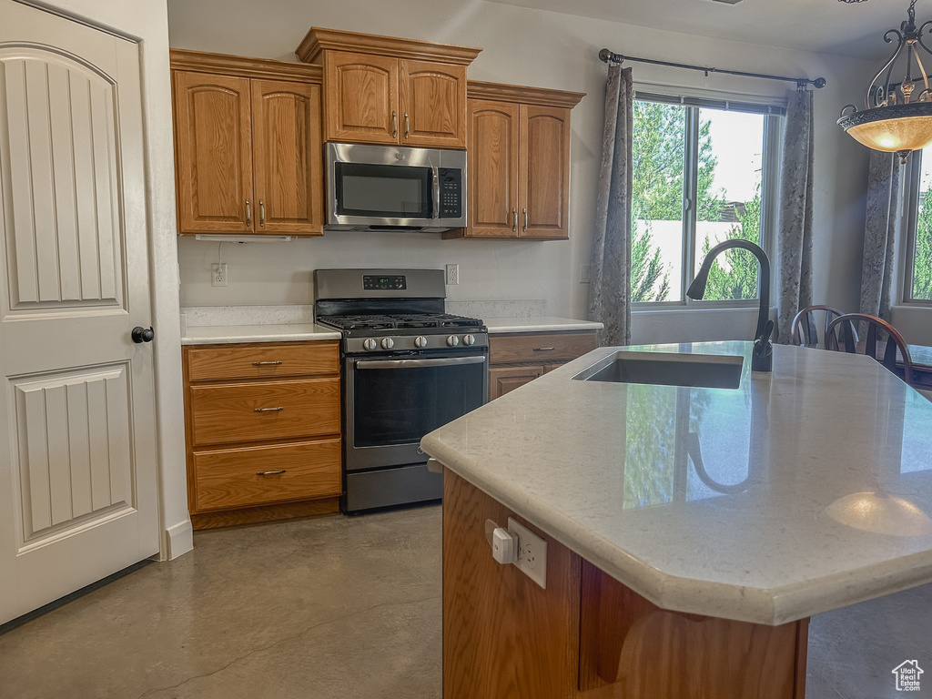 Kitchen with a sink, brown cabinets, concrete flooring, a kitchen island with sink, and stainless steel appliances