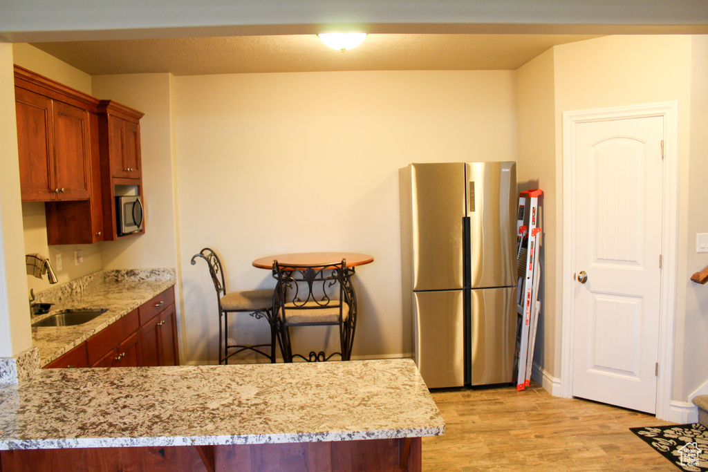 Kitchen with appliances with stainless steel finishes, a sink, light wood-type flooring, brown cabinetry, and light stone countertops