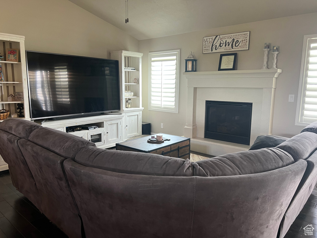 Living room with a glass covered fireplace, dark wood-type flooring, and vaulted ceiling