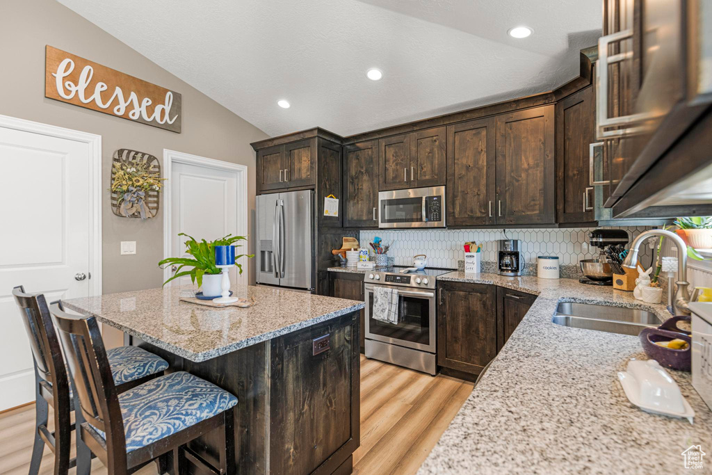 Kitchen featuring lofted ceiling, a kitchen breakfast bar, stainless steel appliances, a sink, and light wood-style floors
