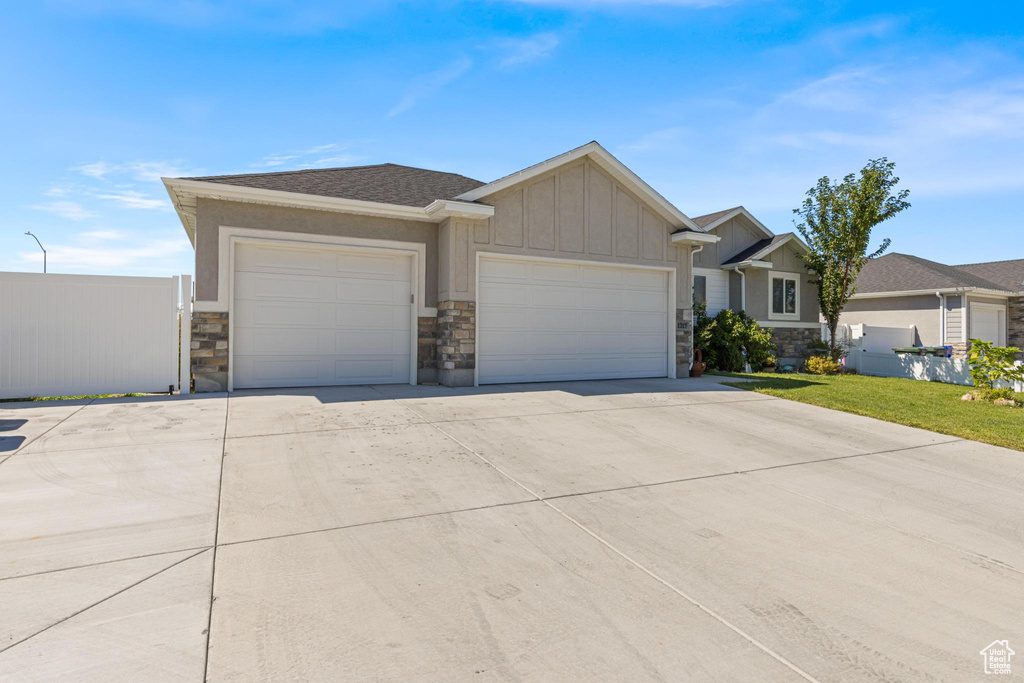 View of front facade with board and batten siding, an attached garage, stone siding, and driveway