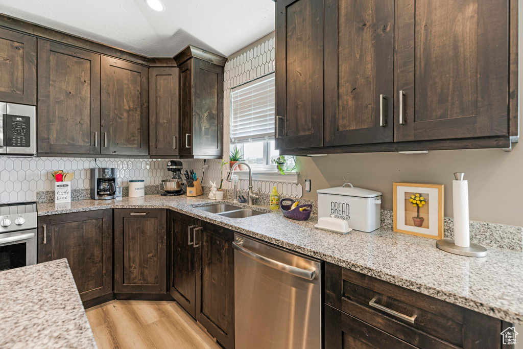Kitchen featuring dark brown cabinets, appliances with stainless steel finishes, light stone counters, and a sink