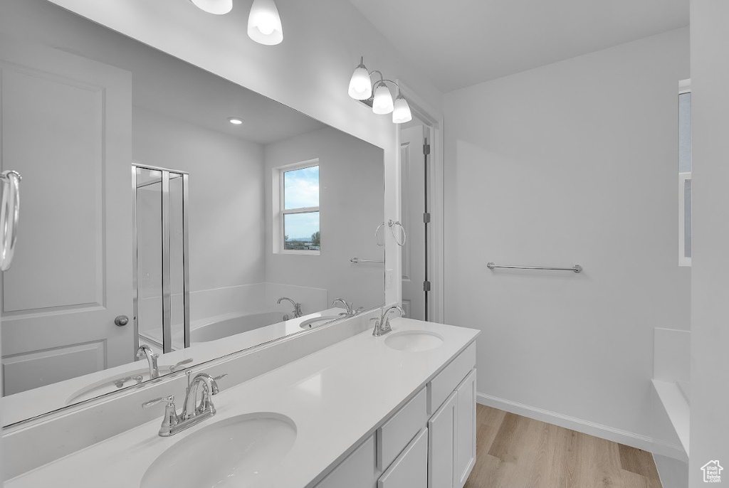 Full bath with wood finished floors, a bath, double vanity, an enclosed shower, and baseboards