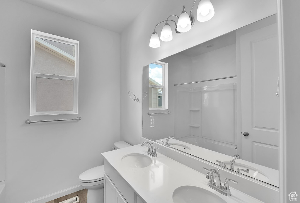 Full bath with toilet, double vanity, wood finished floors, and baseboards