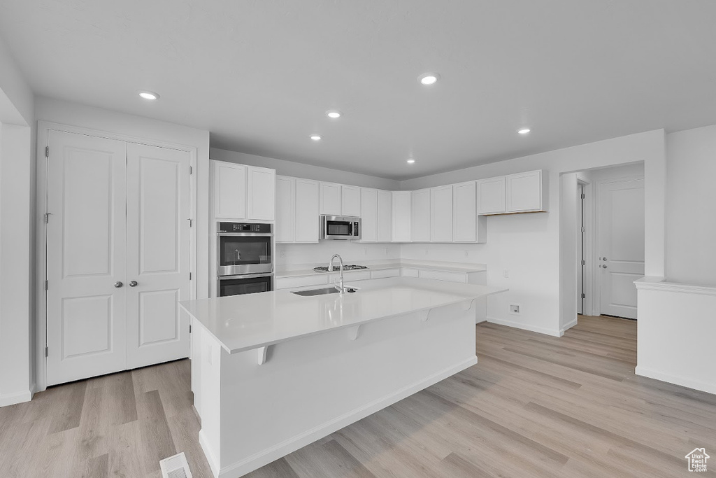 Kitchen featuring appliances with stainless steel finishes, light wood-style flooring, recessed lighting, white cabinetry, and an island with sink