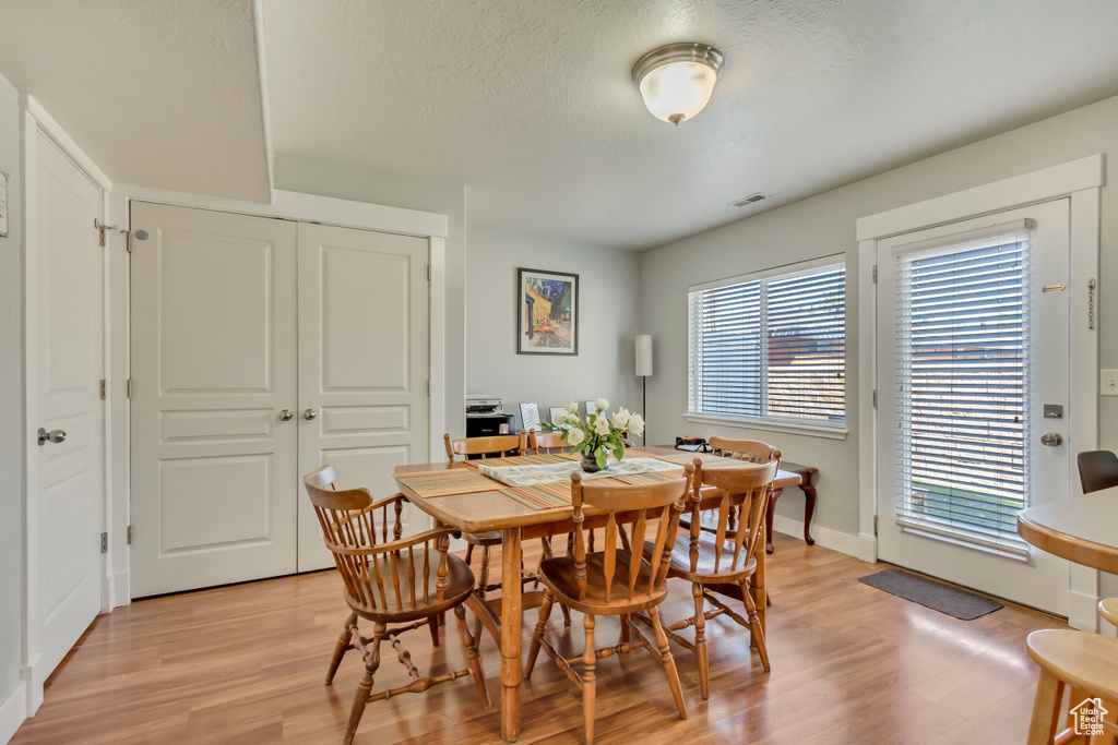 Dining room with baseboards, a textured ceiling, visible vents, and light wood-style flooring