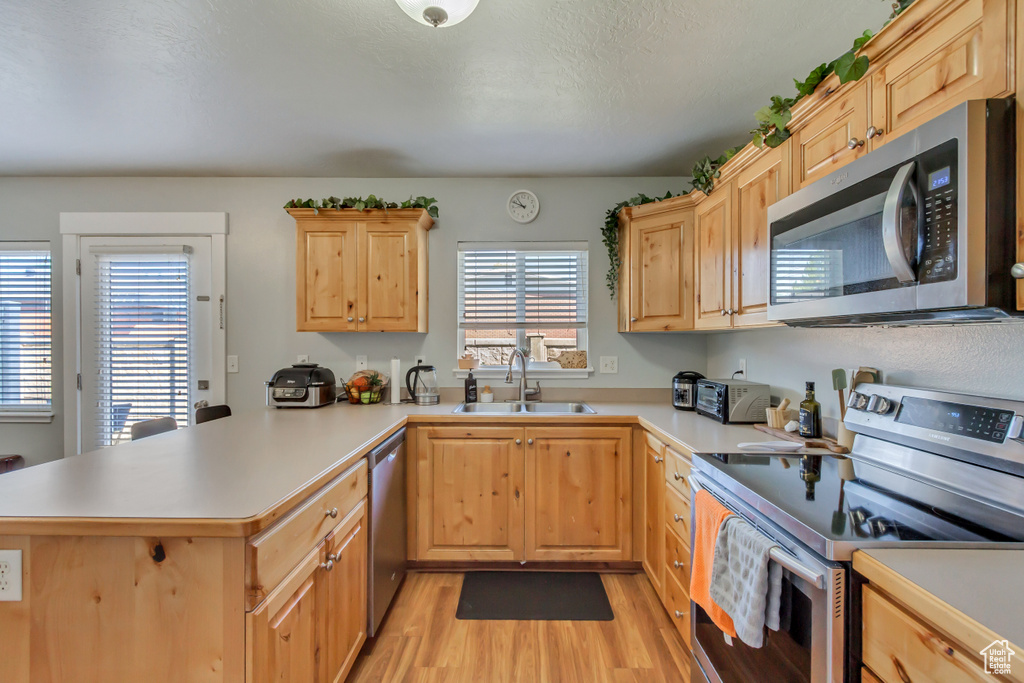 Kitchen featuring a peninsula, light brown cabinets, stainless steel appliances, and a sink