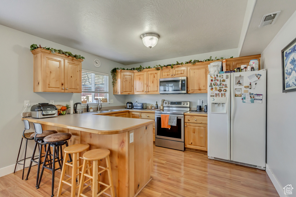 Kitchen with stainless steel appliances, visible vents, light brown cabinets, a sink, and a peninsula