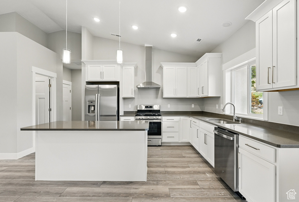 Kitchen featuring stainless steel appliances, wall chimney range hood, a sink, dark countertops, and vaulted ceiling