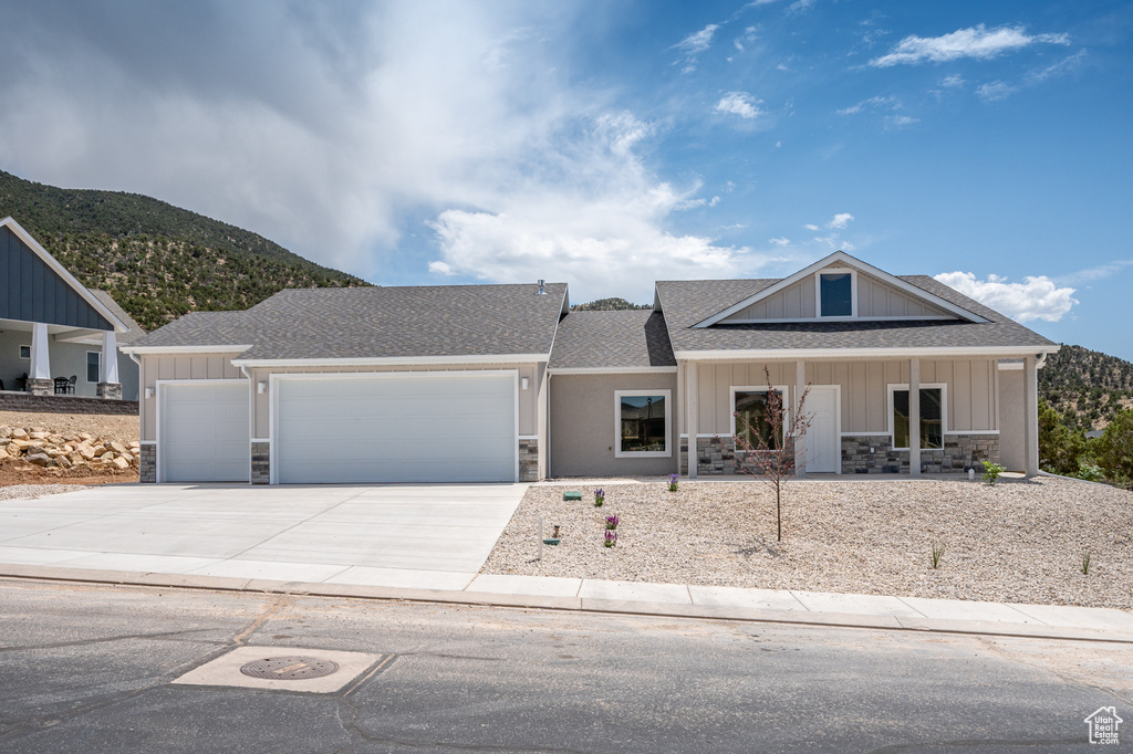 View of front of house featuring stone siding, an attached garage, driveway, roof with shingles, and a mountain view
