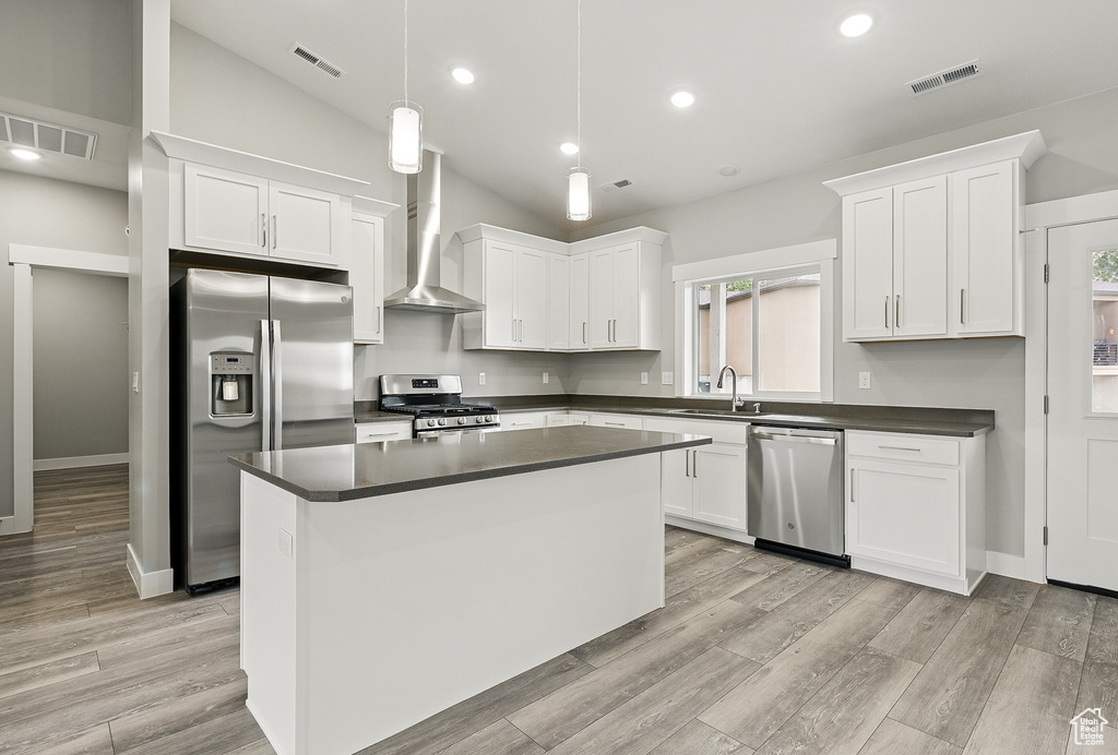 Kitchen featuring stainless steel appliances, wall chimney exhaust hood, a sink, dark countertops, and white cabinetry