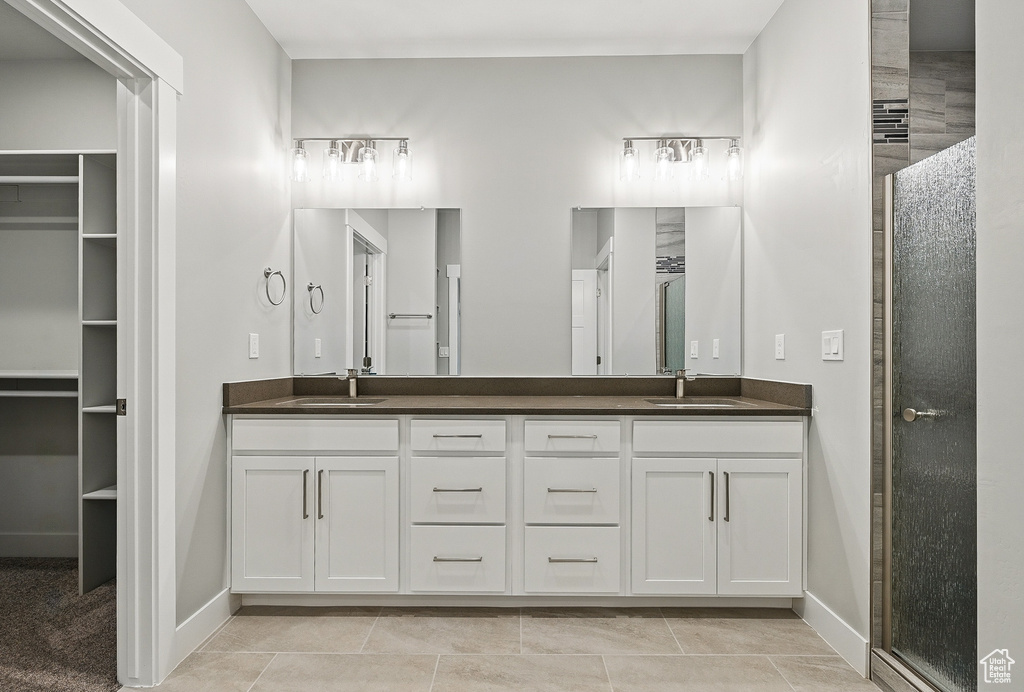 Full bathroom featuring double vanity, a shower stall, baseboards, and a walk in closet