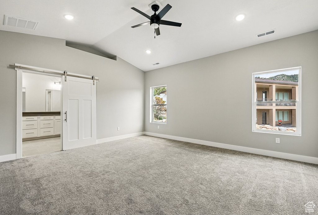 Spare room with a barn door, light carpet, a ceiling fan, lofted ceiling, and baseboards