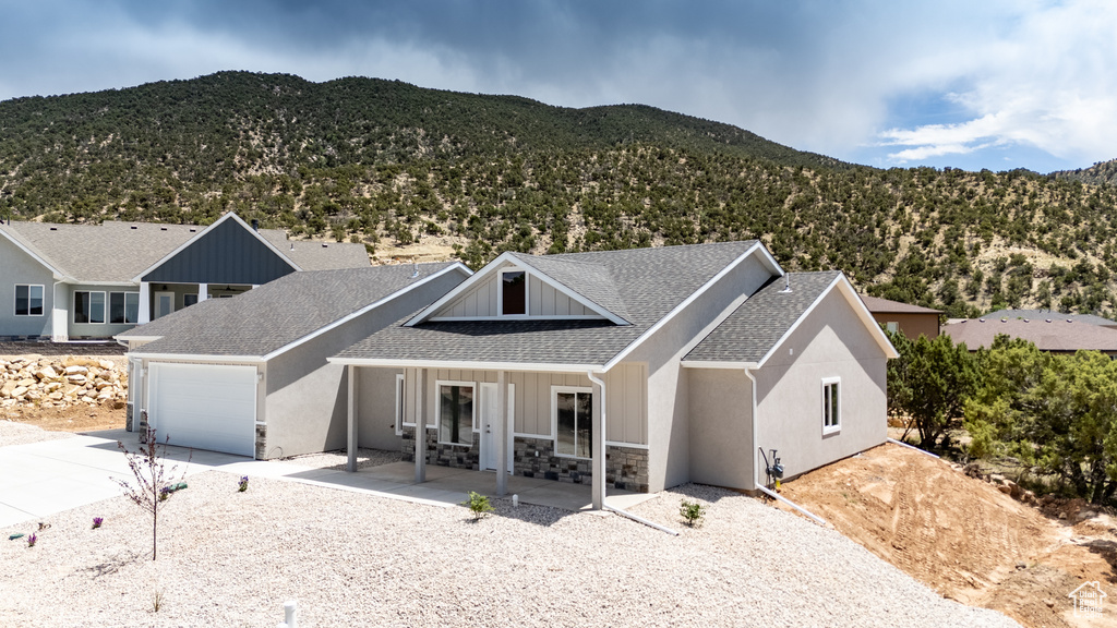 View of front facade featuring driveway, a mountain view, a shingled roof, an attached garage, and stone siding