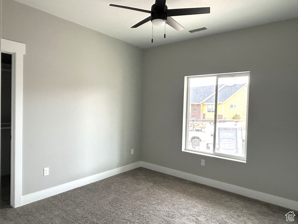 Carpeted empty room with baseboards, visible vents, and ceiling fan