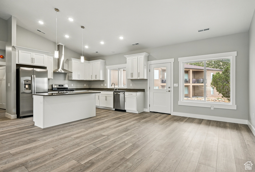 Kitchen with appliances with stainless steel finishes, wall chimney range hood, dark countertops, light wood-style floors, and white cabinets