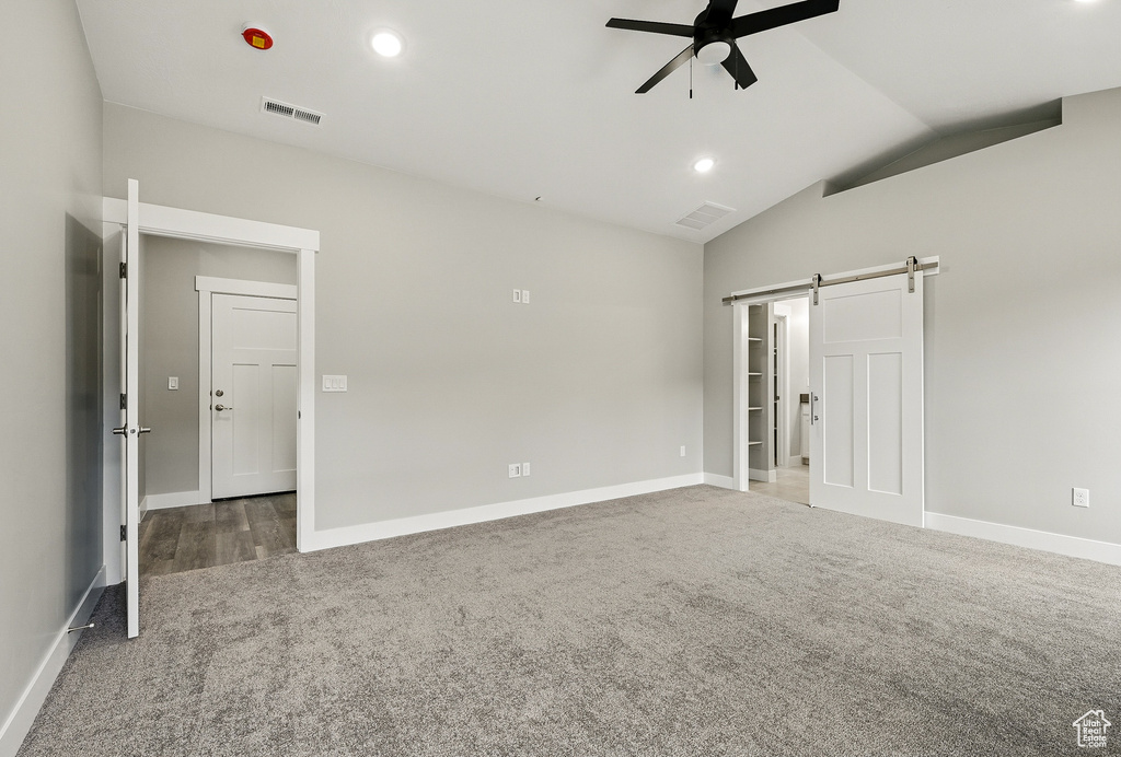 Unfurnished bedroom with a barn door, carpet flooring, vaulted ceiling, baseboards, and ceiling fan