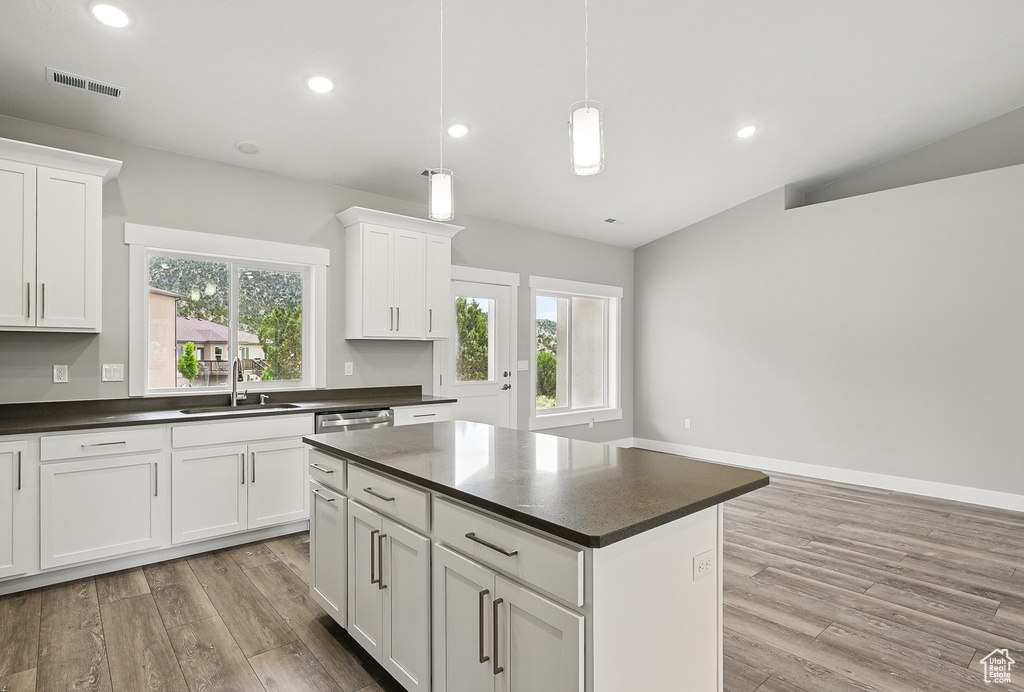 Kitchen with a sink, dark countertops, light wood-style floors, white cabinets, and vaulted ceiling