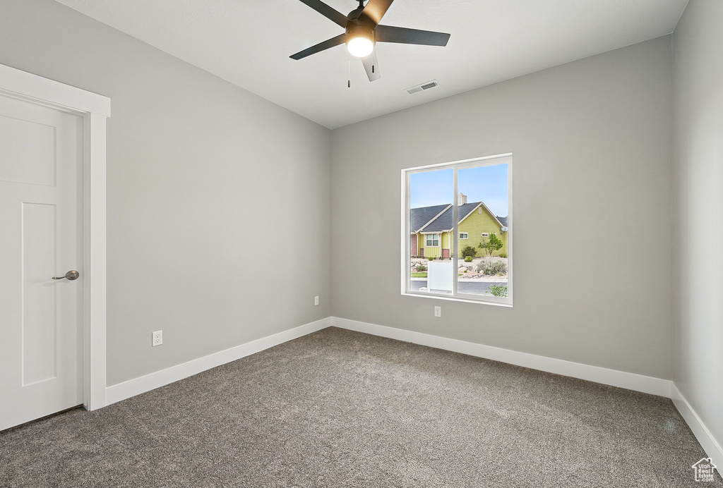 Unfurnished room with dark carpet, baseboards, and a ceiling fan
