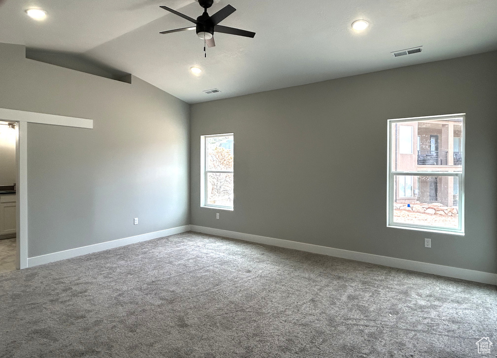 Carpeted empty room with a ceiling fan, visible vents, and plenty of natural light