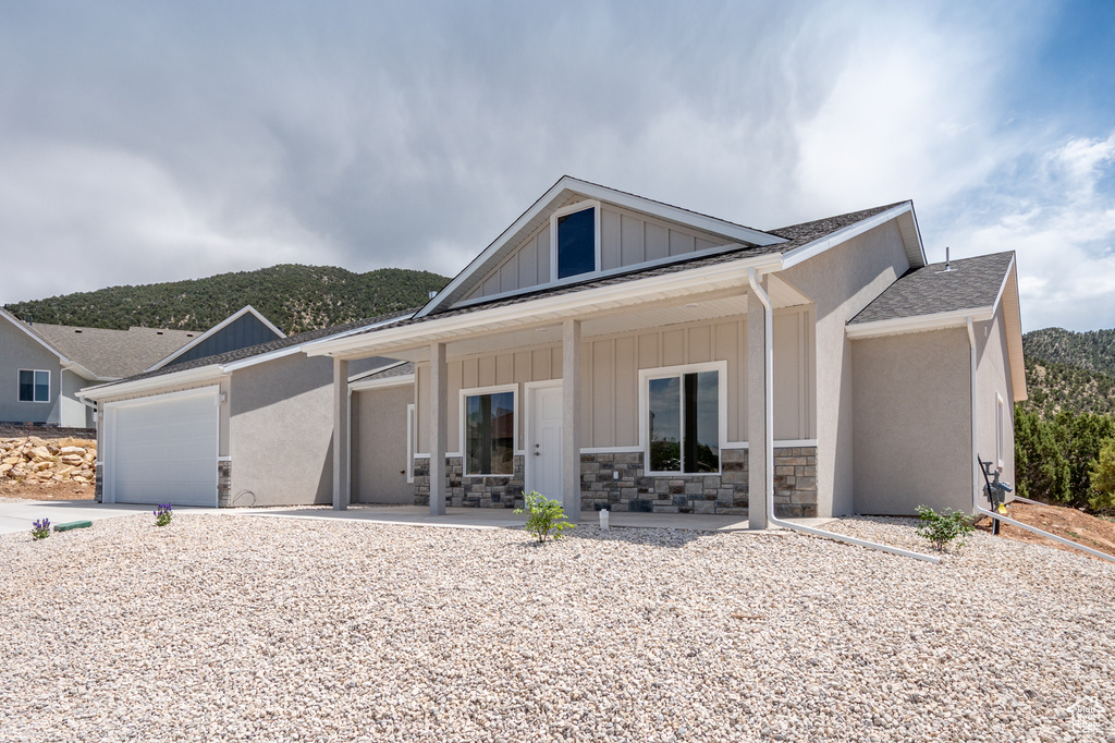 View of front facade featuring covered porch, board and batten siding, driveway, a garage, and roof with shingles