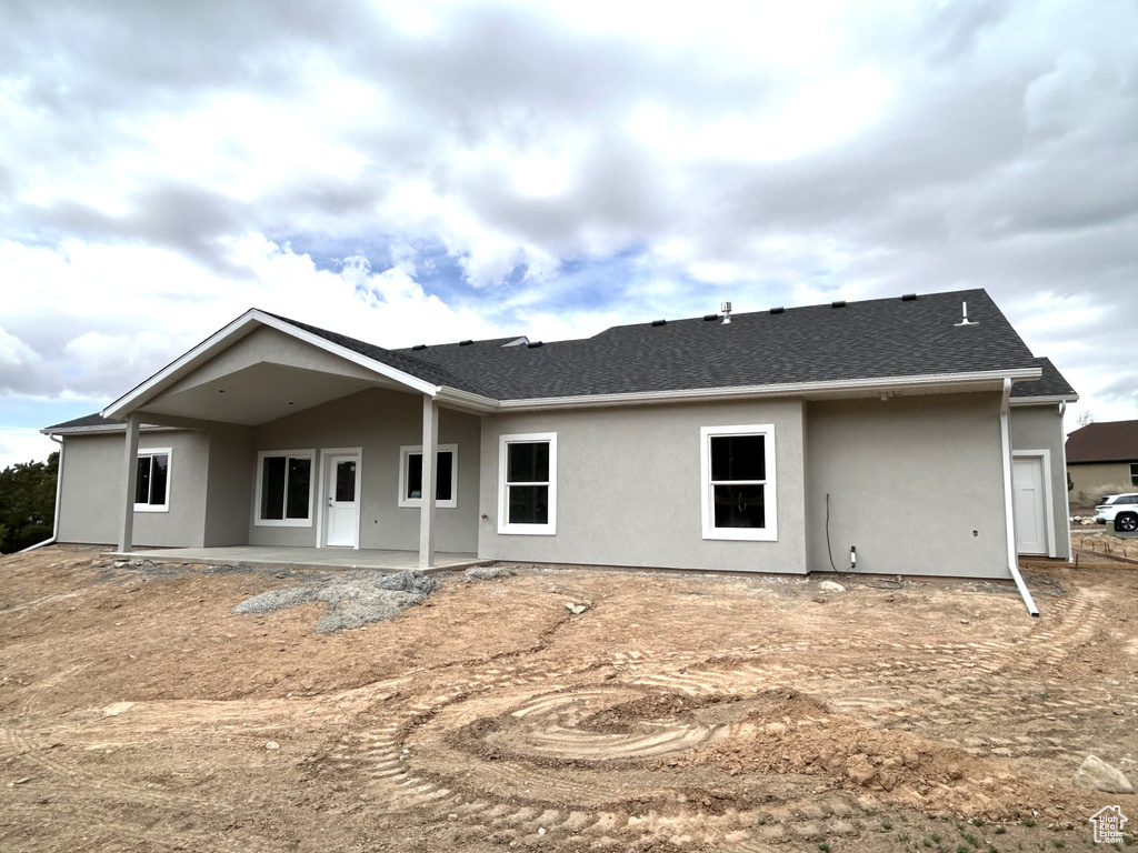 Rear view of property with stucco siding, roof with shingles, and a patio area