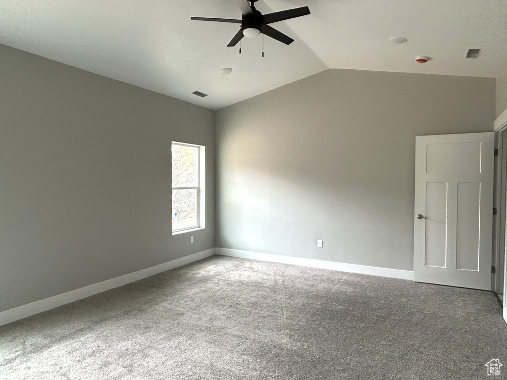 Carpeted spare room featuring vaulted ceiling, visible vents, baseboards, and ceiling fan