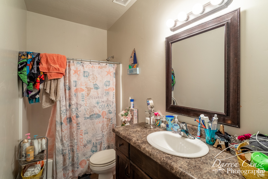 Bathroom featuring toilet, vanity, a shower with shower curtain, and visible vents
