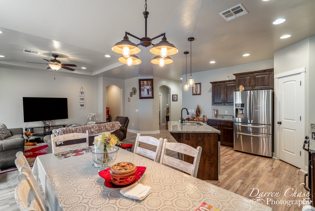 Dining space with arched walkways, light wood-style floors, visible vents, and ceiling fan with notable chandelier