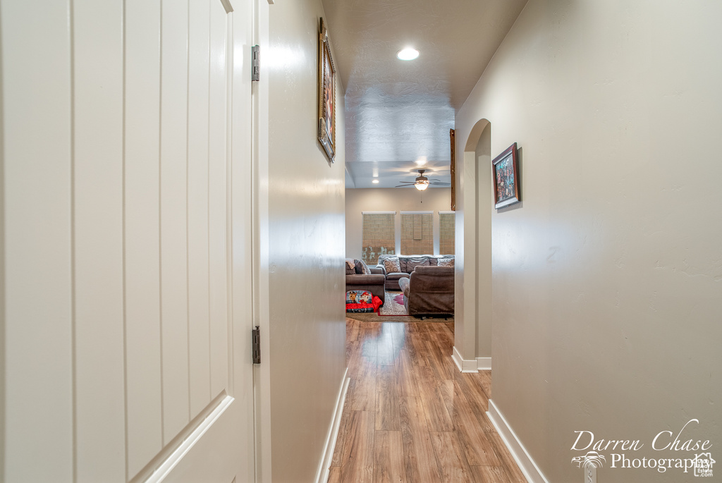 Hall featuring arched walkways, baseboards, and light wood finished floors