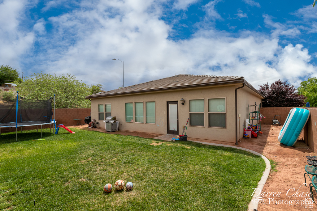 Back of property featuring a tile roof, a fenced backyard, a trampoline, a yard, and stucco siding