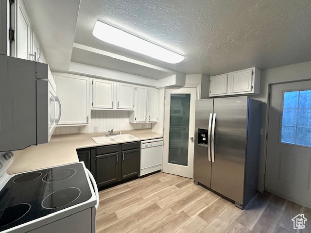 Kitchen with a textured ceiling, white appliances, light wood finished floors, light countertops, and white cabinetry