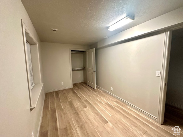 Unfurnished bedroom featuring a textured ceiling, a closet, light wood-style floors, baseboards, and visible vents