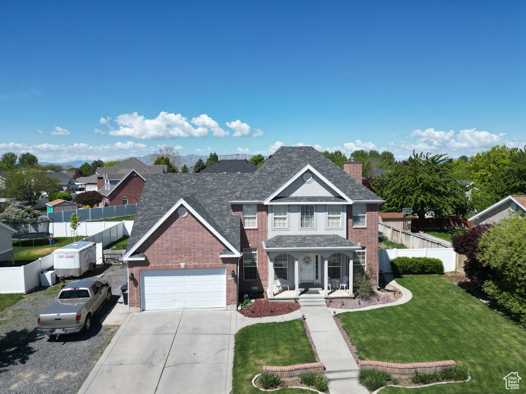 Traditional home featuring covered porch, fence, concrete driveway, a front yard, and brick siding