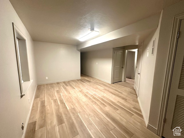 Finished basement with light wood finished floors, baseboards, and a textured ceiling