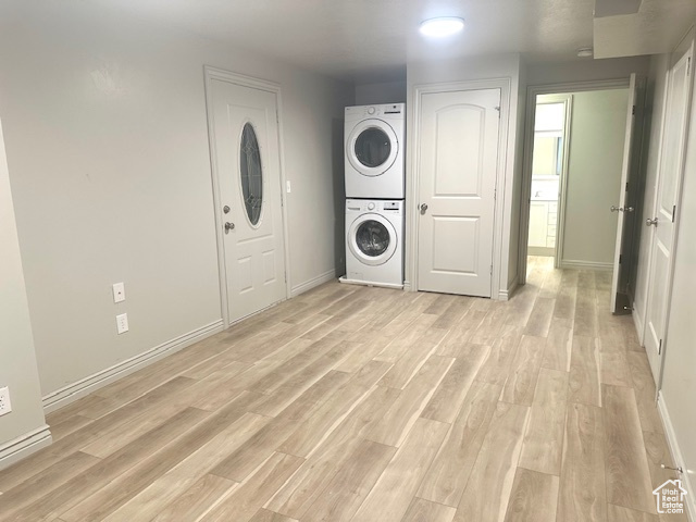 Laundry room featuring baseboards, stacked washer / dryer, laundry area, and light wood-type flooring