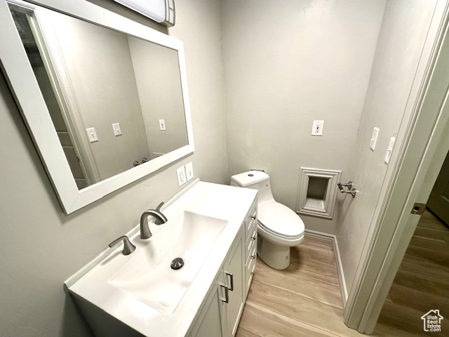 Half bathroom featuring baseboards, wood finished floors, toilet, and vanity